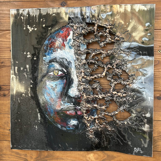 Tableau contemporain en métal de Philippe Buil représentant un visage en relief, moitié peint avec des pigments, moitié ajouré en dentelle d’acier et de bronze, créant un jeu d’ombres et de lumière.