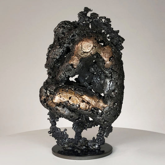 Sculpture de Philippe Buil représentant un corps d'homme accroupi intégré à une forme évoquant une montagne. Sculpture en dentelle de métal : acier et bronze.