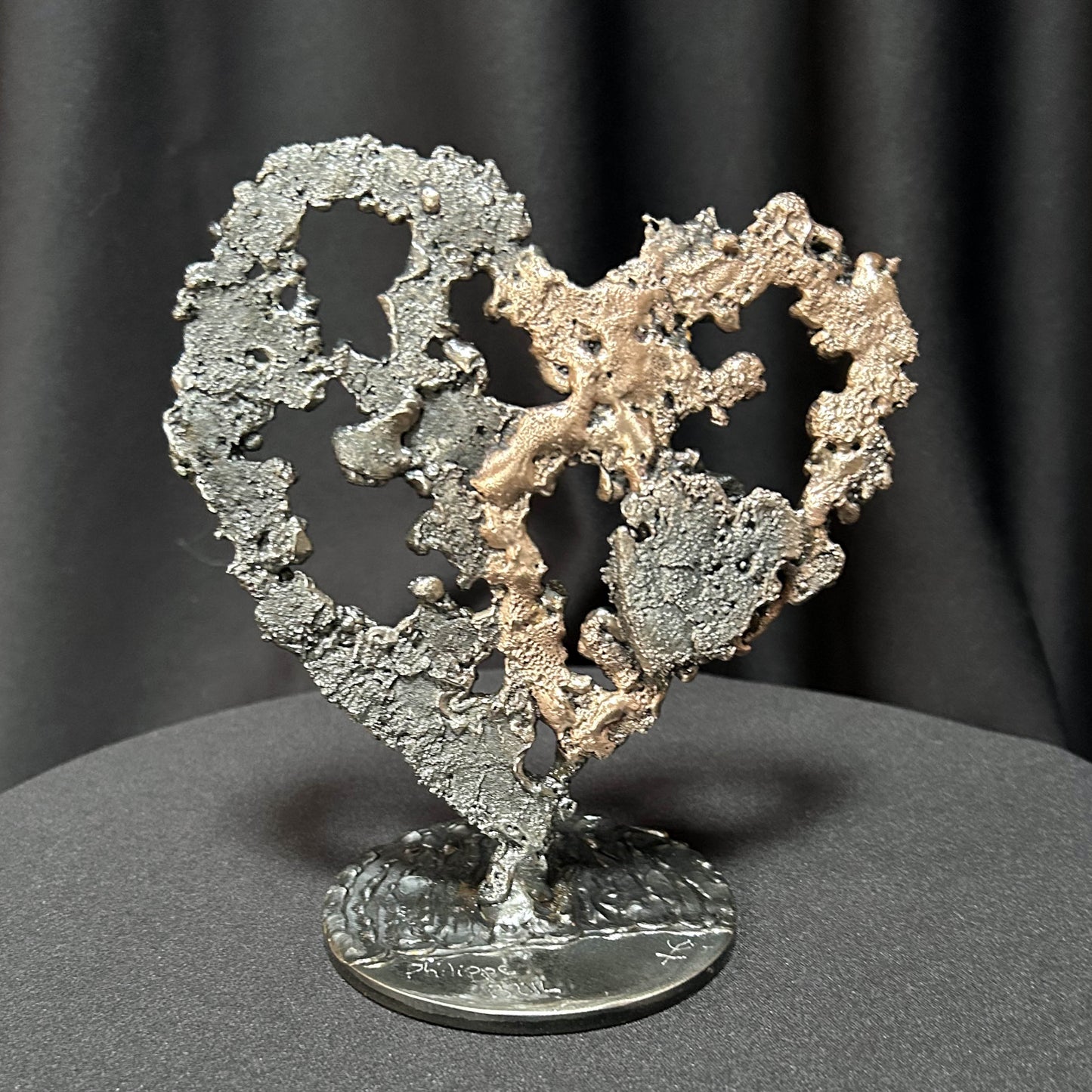 Sculpture de cœur en dentelle de métal noir et bronze par Philippe Buil, vue de face sur socle circulaire.