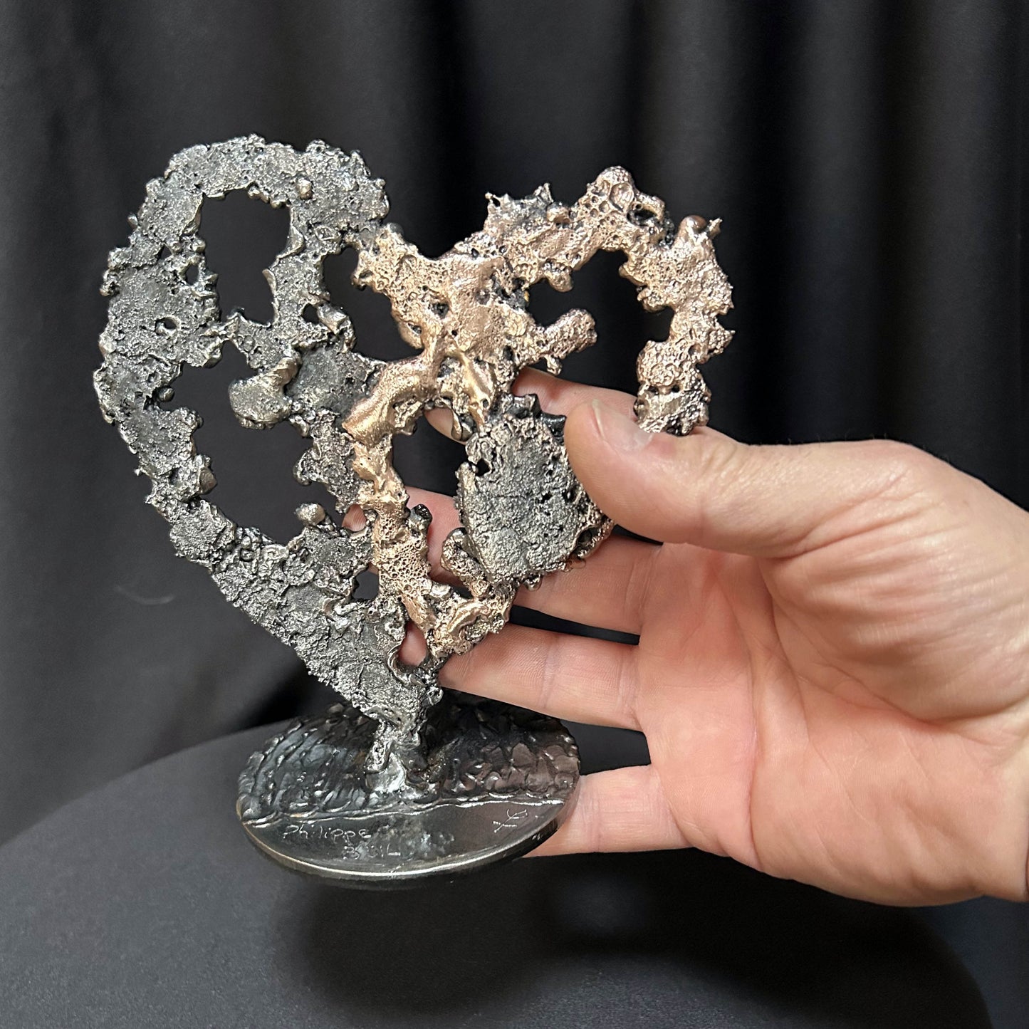 Sculpture de cœur en dentelle de métal noir et bronze par Philippe Buil, dans les mains de l'artiste
