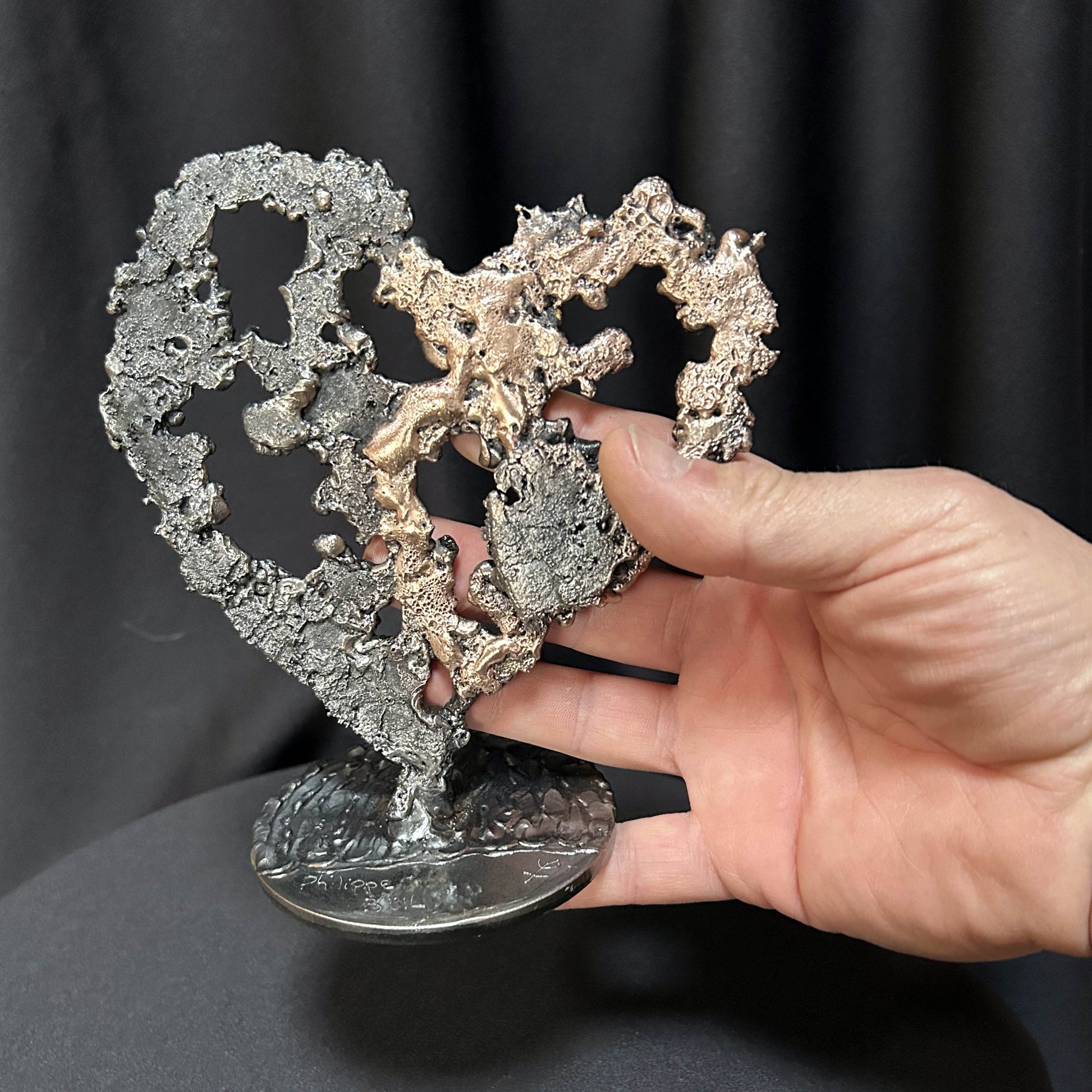 Sculpture de cœur en dentelle de métal noir et bronze par Philippe Buil, dans les mains de l'artiste