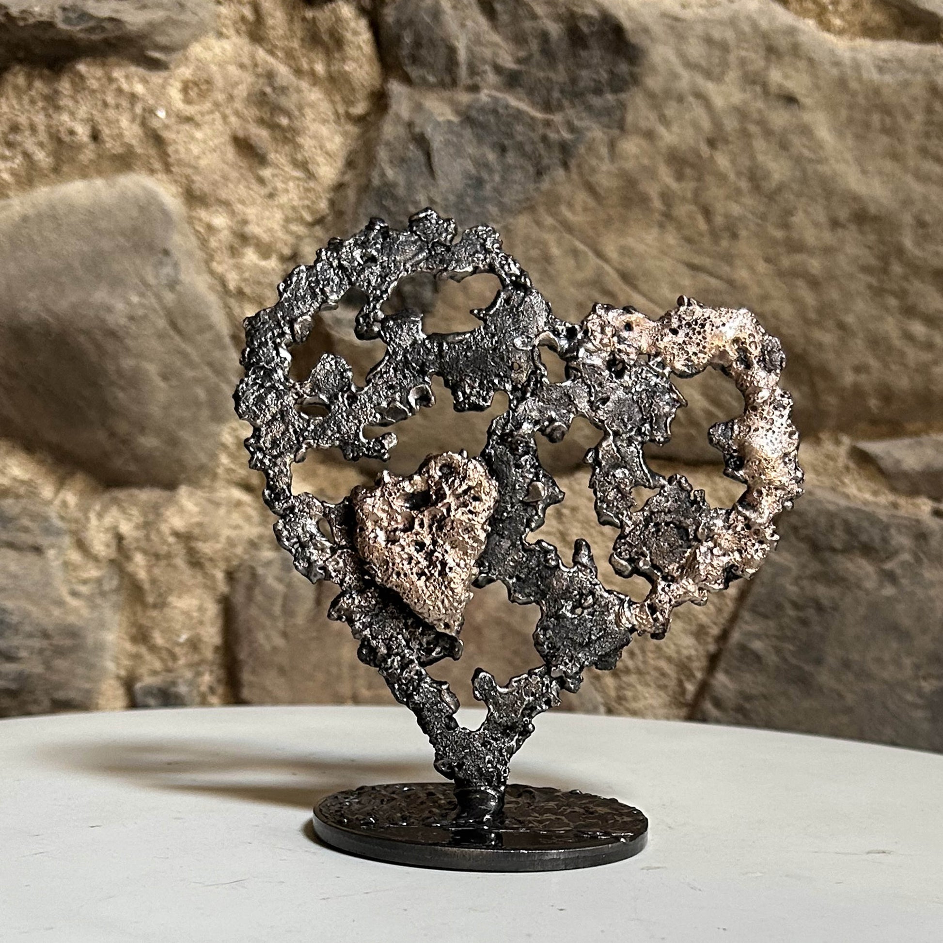 Sculpture coeur en acier et bronze - Dentelle de métal de Philippe Buil sur mur en pierre