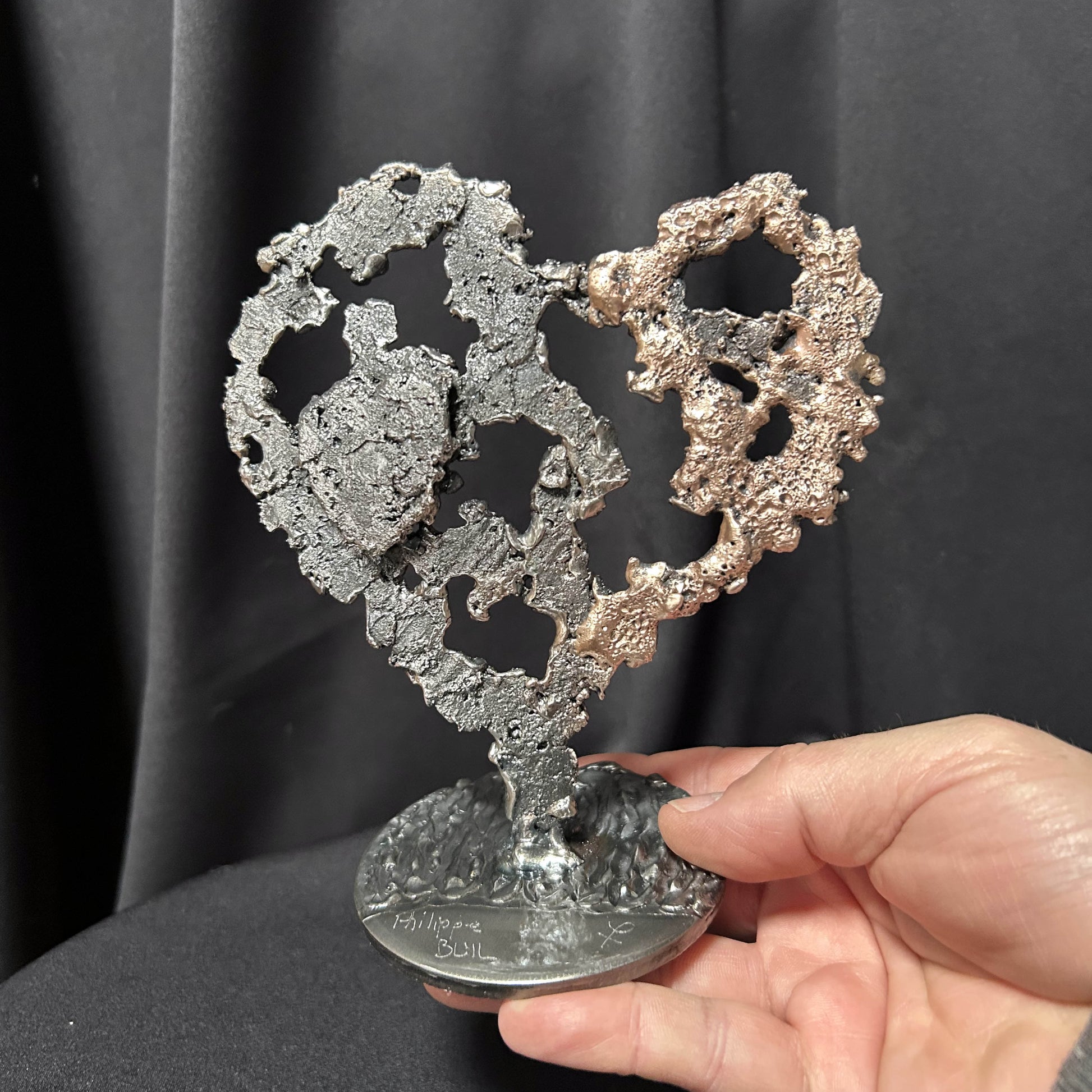 Main de l'artiste présentant sa sculpture en forme de coeur en dentelle de métal