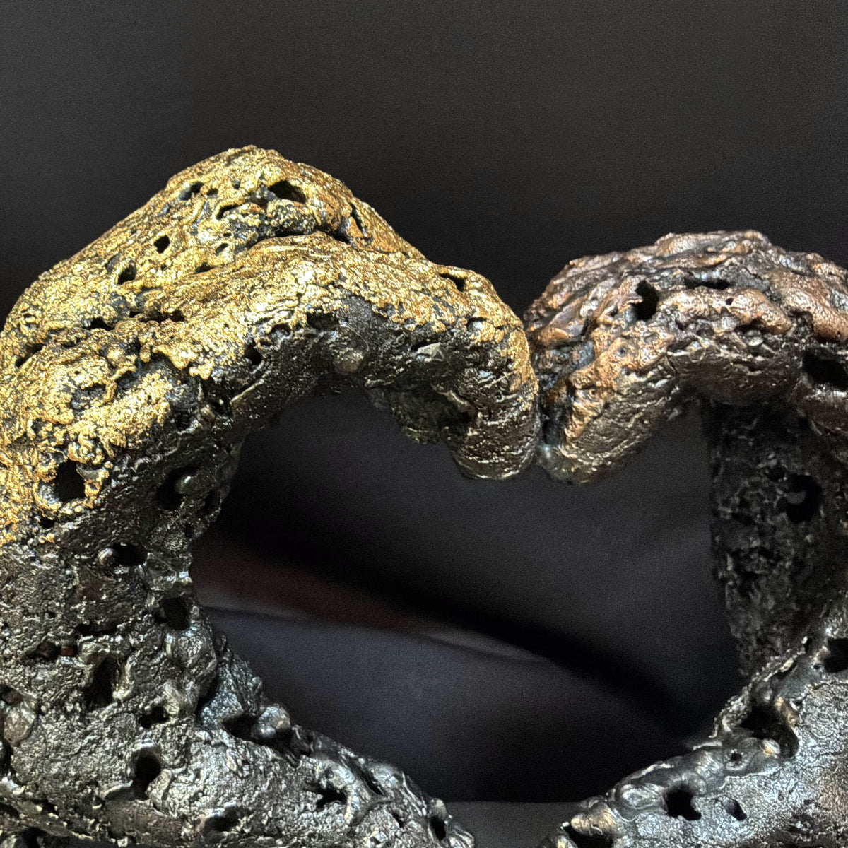 Détail du cœur formé par les deux mains en dentelle de métal, entre pleins, vides et reliefs