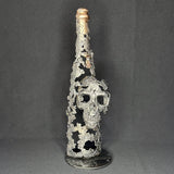 Sculpture en dentelle de métal représentant une tête de mort intégrée à une bouteille de vin, réalisée en acier et bronze par Philippe Buil.