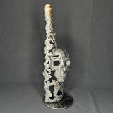 Sculpture en dentelle de métal représentant une tête de mort intégrée à une bouteille de vin, réalisée en acier et bronze par Philippe Buil.