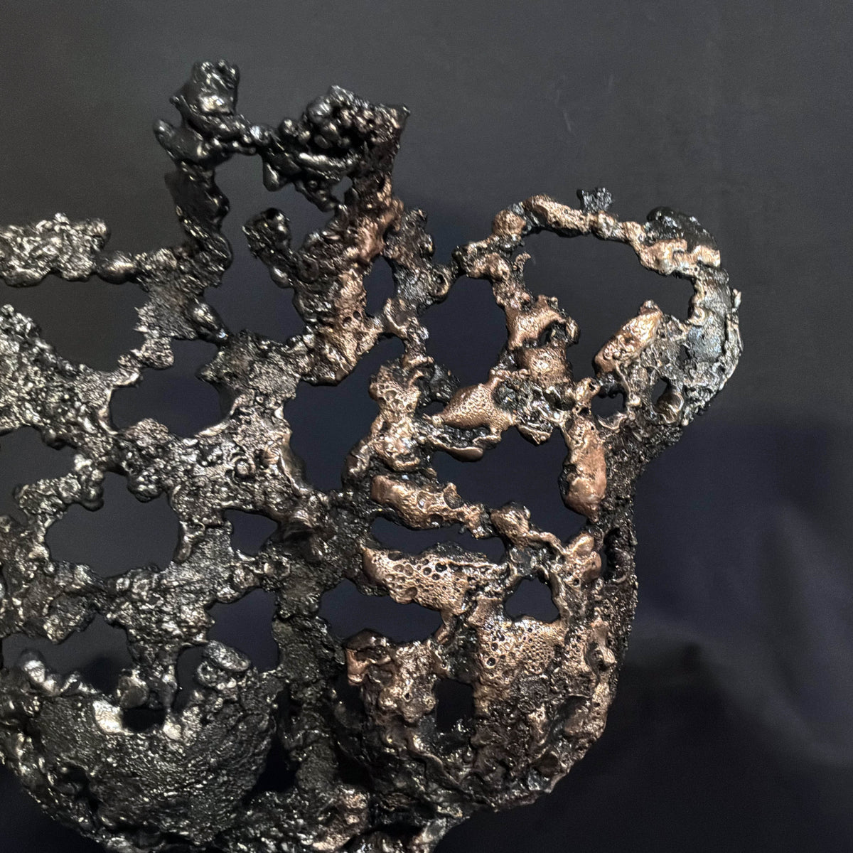 Gros plan sur les nuances bronze de la sculpture Les Signes de Demain et les contrastes entre métal sombre et reflets chauds.