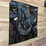 Sculpture murale de Philippe Buil sur tôle d’acier découpée, dentelle de métal et pigments : un chat arlequin expressif au regard bleu hypnotique.