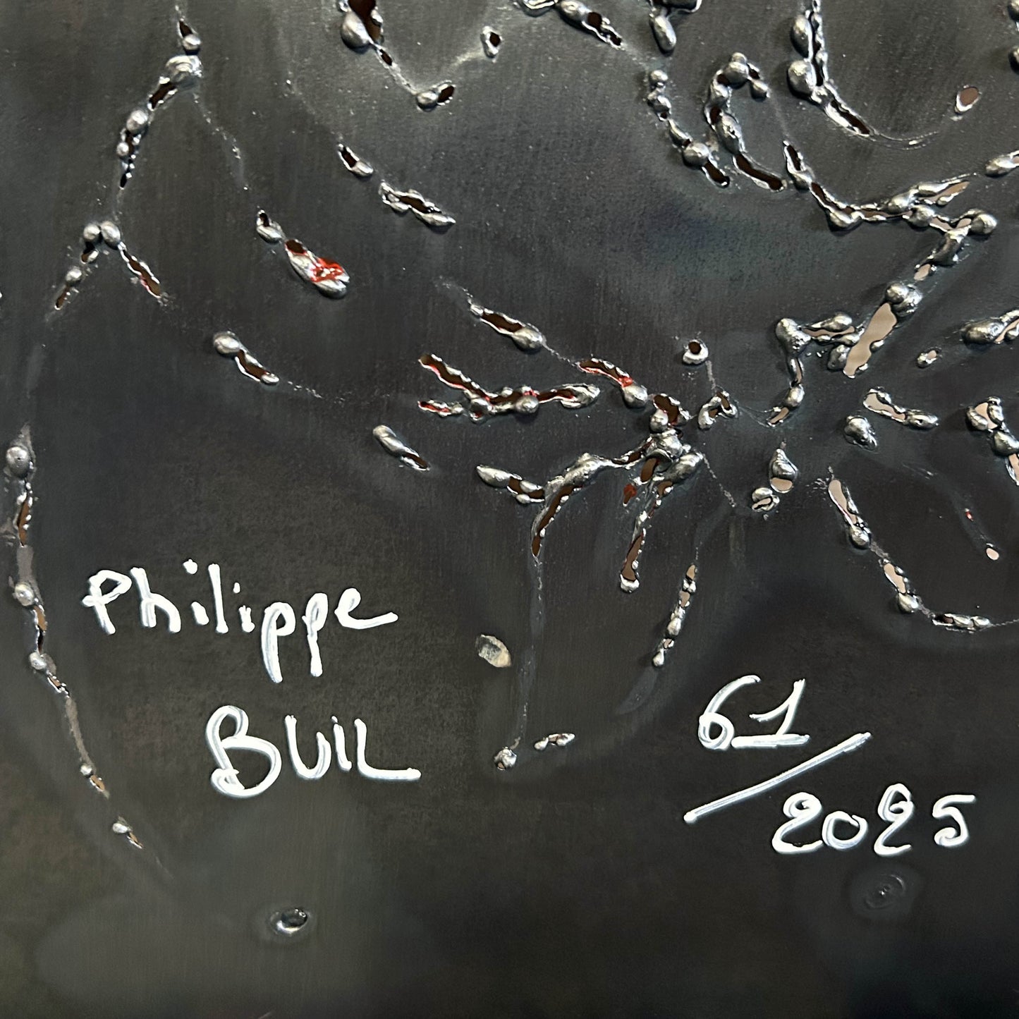 Sculpture murale en métal de Philippe Buil représentant un chien portant un béret et un foulard basque, avec pigments colorés et fond texturé sombre