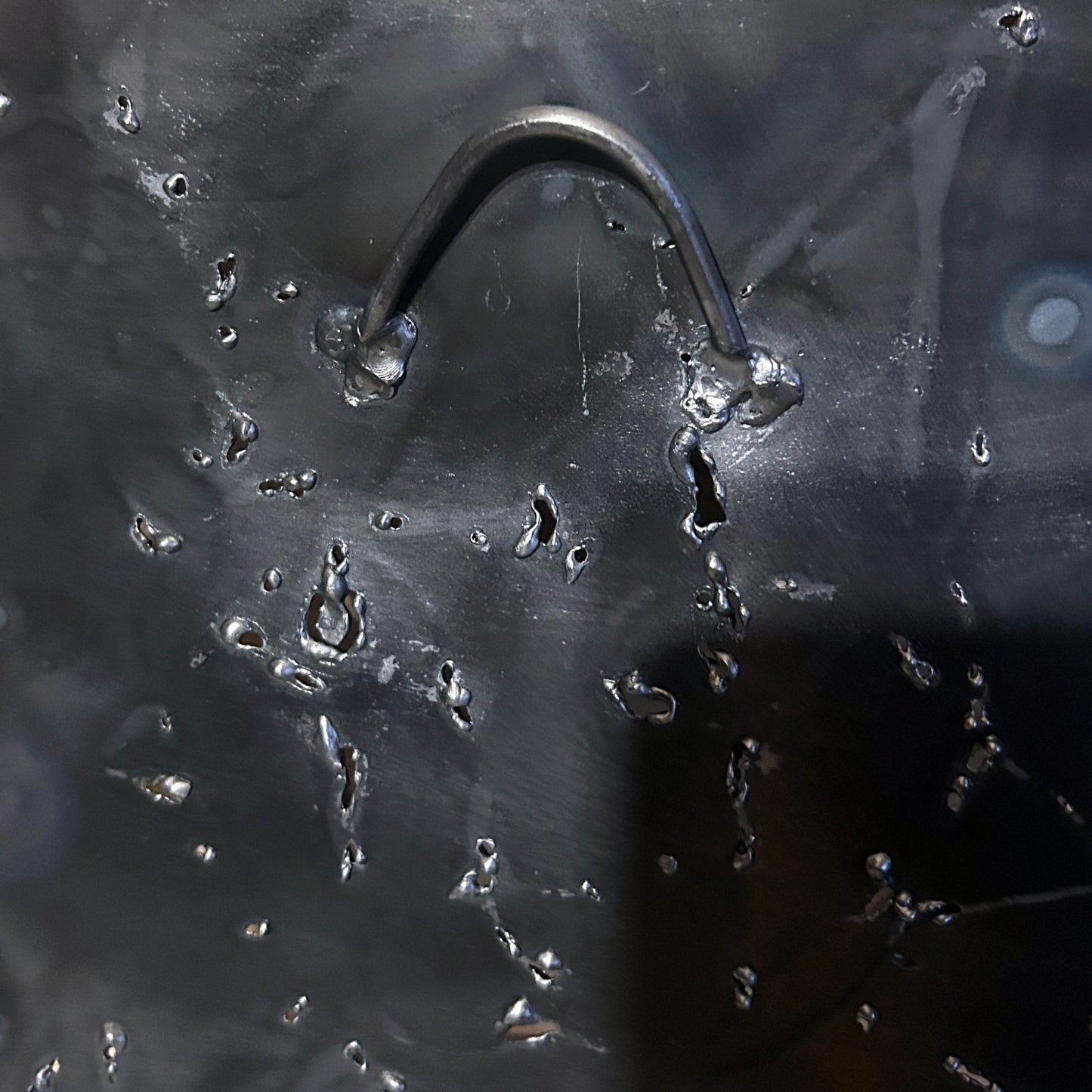 Sculpture murale carrée de 25x25 cm représentant un chat arlequin aux yeux bleus intenses, portant une collerette blanche et un chapeau rayé rouge et jaune. L’œuvre est réalisée en acier texturé et pigments, avec un fond gris brumeux et métallisé