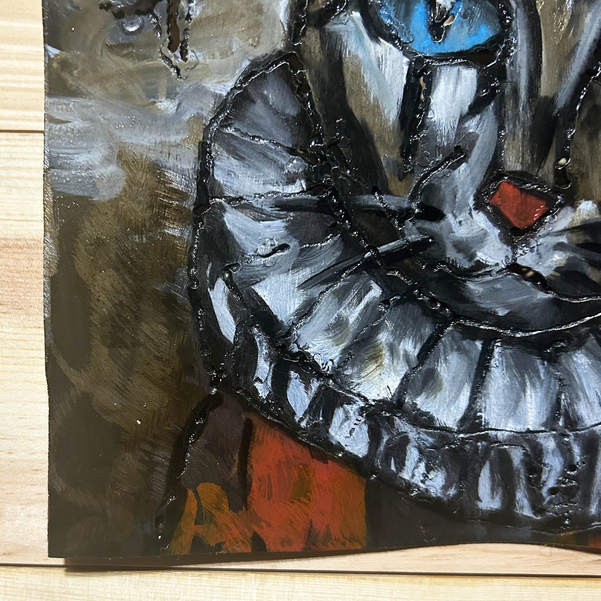 Sculpture murale carrée de 25x25 cm représentant un chat arlequin aux yeux bleus intenses, portant une collerette blanche et un chapeau rayé rouge et jaune. L’œuvre est réalisée en acier texturé et pigments, avec un fond gris brumeux et métallisé