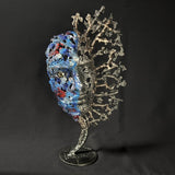 Sculpture de Philippe Buil représentant un visage humain en dentelle d'acier et bronze. Le côté gauche du visage est coloré avec des pigments bleus et rouges, tandis que le côté droit se transforme en une structure métallique ajourée et arborescente.
