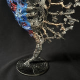 Sculpture de Philippe Buil représentant un visage humain en dentelle d'acier et bronze. Le côté gauche du visage est coloré avec des pigments bleus et rouges, tandis que le côté droit se transforme en une structure métallique ajourée et arborescente.