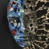 Sculpture de Philippe Buil représentant un visage humain en dentelle d'acier et bronze. Le côté gauche du visage est coloré avec des pigments bleus et rouges, tandis que le côté droit se transforme en une structure métallique ajourée et arborescente.